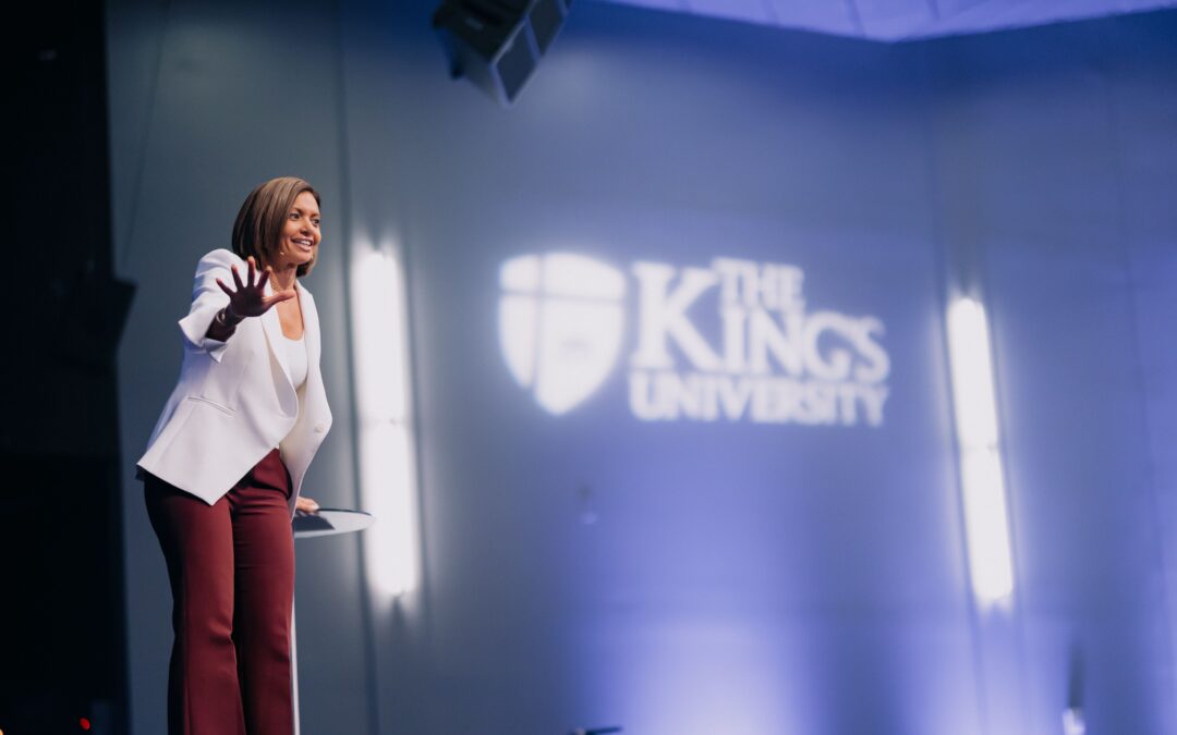 Dr. Irini Fambro teaching from stage at Chapel at The King's. TKU logo in the background.